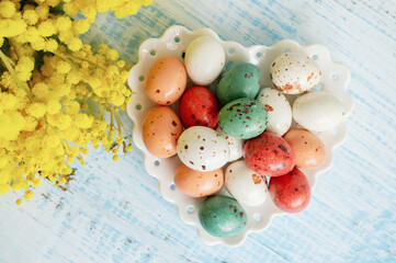 easter eggs with mimosa. Easter holiday mimosa flowers decorated with colorful eggs. Chocolate candies with frosting in the form of quail eggs on a wooden background