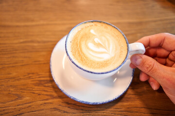 A cup of hot cappuccino on the table in the coworking space of the coffee shop. A cup of coffee on the veranda on a sunny day. Coffee break at the cafe. Close-up