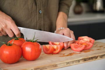 Unrecognizable young man cutting tomatoes on a chopping board at kitchen.
