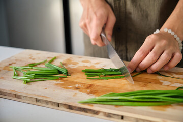 Obraz na płótnie Canvas Close up of young man hands cutting chinese chive on a chopping board at kitchen.