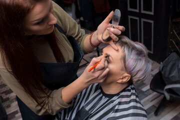 Fototapeta premium Brunette girl, adult, pretty, European, making up and dyeing eyebrows to a female client at work in a barbershop