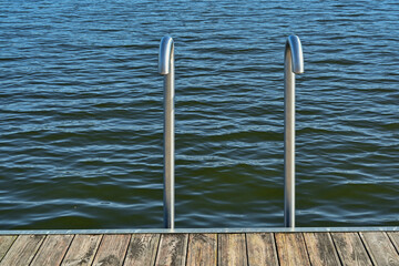 Steel handrails of a staircase into the water on a wooden pier by the summer lake