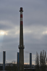 Fototapeta na wymiar Industrial buildings and old disused chimney with mobile antennas on cloudy sky background.