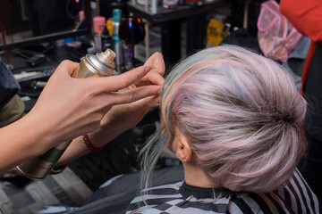 Fototapeta premium The girl's hands of a professional hairdresser-stylist-make-up artist hold the varnish and straighten the hair of a stylish, fashionable hairstyle color coloring creative bob