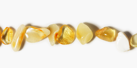 Amber stones at sunlight on light background, transparent stone yellow beige color. Natural texture gemstone mineral material, healing crystal. Top view Amber in row as banner. Nature gems