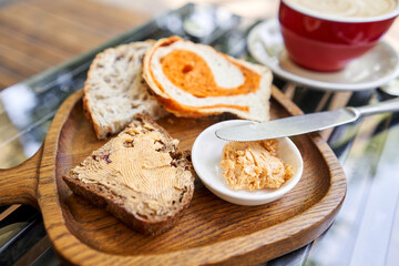 A slice of bread with butter on a chopping board. Assorted sliced bread on a wooden board. Served with smoked butter. Breakfast with cappuccino coffee. 