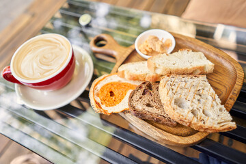 Assorted sliced bread on a wooden board. Served with smoked butter. Breakfast with cappuccino coffee. Composition with butter and bread on wooden plate.