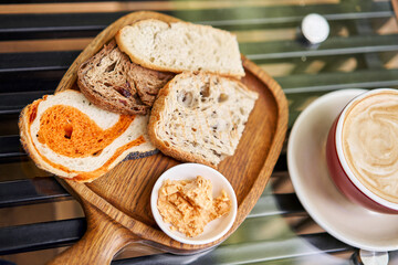 Assorted sliced bread on a wooden board. Served with smoked butter. Breakfast with cappuccino coffee. Composition with butter and bread on wooden plate.