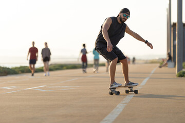 Fototapeta premium Adult attractive man in black clothes skating on the street by the beach