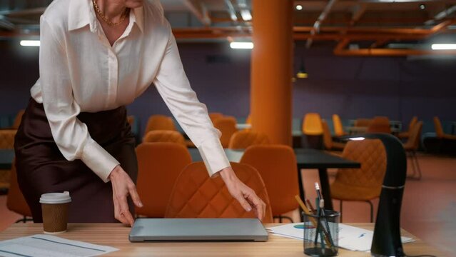 Confident classy caucasian blonde mature woman 50s sitting at deck, opening and typing on laptop.Mature female professional writing an important email in open space loft office,modern co working space