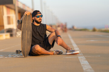 A cool guy sitting on a road with a skateboard © KONSTANTIN SHISHKIN