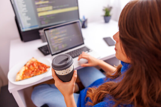 Female programmer drinking coffee and eating pizza while working remotely from home