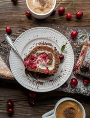 Slice of black forest cake roulade on a plate on wooden background