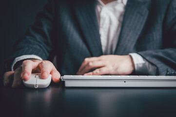 Close up of businessman hand using mouse and typing on computer keyboard sitting working on office workplace desk or work from home with copy space background. Business people and technologt concept.