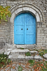 Fototapeta na wymiar Exquisite blue wooden door of a entirely stone-built house with an apotropaic symbol above the door. Found in the village of Kalarrytes, in the mountainous region of Tzoumerka, in Greece, Europe.