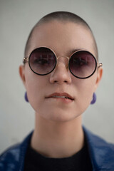 Close up portrait of a fashionable short hair young female in circular sunglasses biting her lips. 