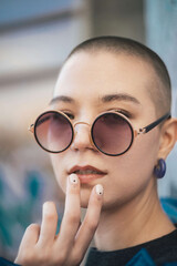 Close up portrait of a fashionable short hair young female in circular sunglasses gently touching her lips. 