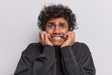 Young curly haired Hindu man in his 20s wears casual black t shirt expresses sense of confusion and uncertainty spreads palms cannot answer your difficult question isolated over white background