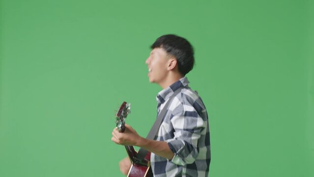 Side View Of Young Asian Teen Boy Playing Guitar With Rock Music On The Green Screen Background
