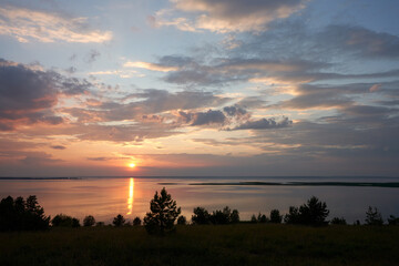 Panoramic scenic view of a full-flowing river at sunset.  The sun descends to the horizon of the...