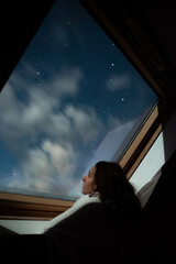 Une femme rêveuse regarde un ciel étoilé à travers une vitre