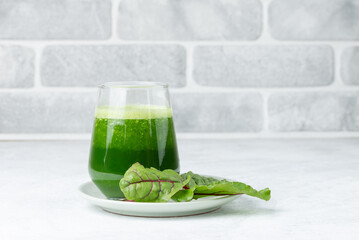 Freshly squeezed juice or smoothie in a glass with fresh chard leaves  on plate on a light table with copy space