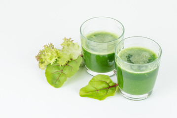 Two glasses with freshly squeezed green  juice or smoothie with fresh lettuce and chard leaves isolated