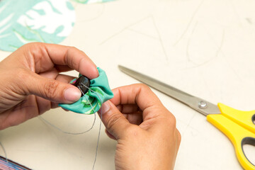 Mãos costurando botão em tecido colorido em mesa de costura linha e agulha e tesoura. São Paulo,...