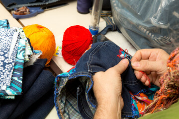 Mãos costurando jeans com linha e agulha. Atelier de costura em São Paulo, Brasil. 