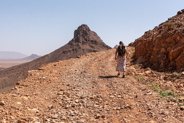 Fototapeta na wymiar Hiking up the mount Zagora on a gravel road, mount Adafane in the background, Draa valley