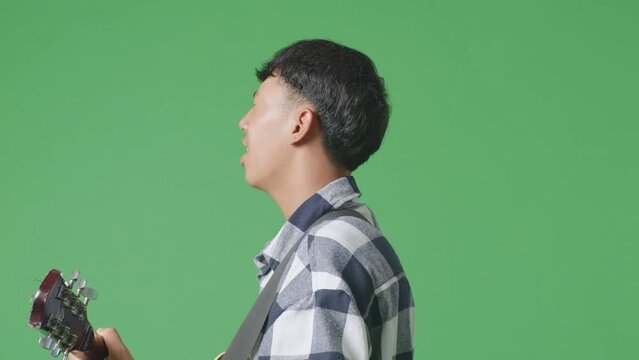 Close Up Side View Of Young Asian Teen Boy Playing Guitar With Rock Music On The Green Screen Background
