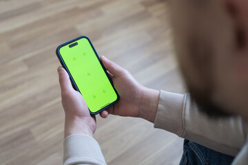 Man at home lying on a couch using smartphone with green mock-up screen, doing swiping, scrolling gestures. Guy using mobile phone, internet social networks browsing. Social media.