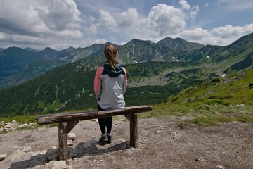 Young girl is sitting on the bench enjoying view of high peaks of Vysoke Tatry mountains near to...