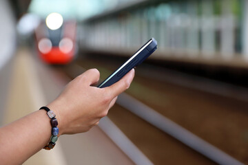 Smartphone in hand of woman waiting for the arriving train on railroad station. Commuter train passenger, online payment for the trip in summer