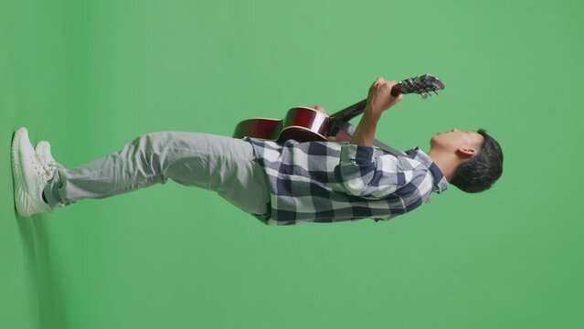 Full Body Side View Of Young Asian Teen Boy Playing Guitar With Rock Music On The Green Screen Background
