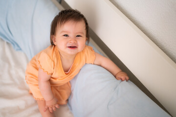 lifestyle home portrait of happy and adorable 9 months old baby girl looking at the camera in funny face expression on white background standing by the bed