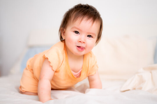 lifestyle home portrait of happy and adorable 9 months old baby girl looking at the camera in funny face expression on white background crawling on bed