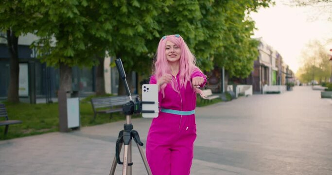 A cheerful girl in pink dances in front of the phone, which she put on a tripod in front of her. Happy flash mob on the street