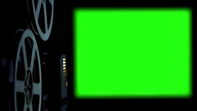 Old Cinema Projector Displays Green Screen. In a dark room you can see parts of the film projector and his wheels that turn.