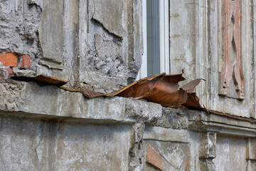 An old broken drainage system under the window, outside the building. Destroyed, rusty drainage.