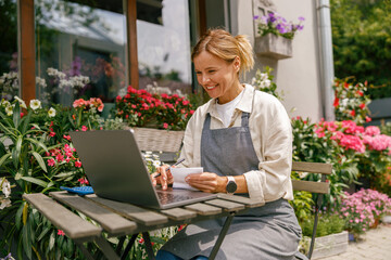 Beautiful flower shop owner wearing apron working on laptop in her store