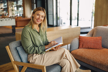 Smiling woman manager sitting on chair in coworking and making notes during working day