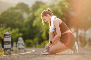 Female runner kneeling and tying shoelace on the street. Fitness woman tying shoelaces. Young woman runner tying shoelaces in park with sunset and sunbeam.