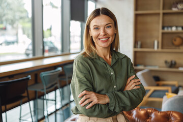 Female entrepreneur standing with crossed hands on coworking space background and looking camera