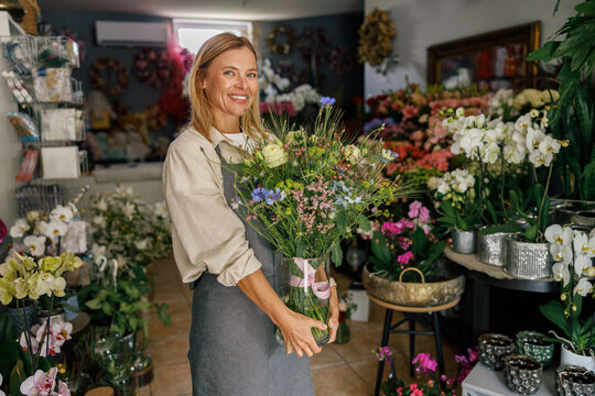 Attractive woman flower shop owner in apron holding bouquet of flowers at florist store