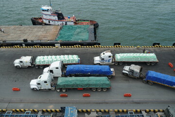 Fully loaded trucks with bags of fertilizer approaching the pier for manual discharging by...
