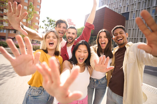 Cheerful multicultural group of friends waving happy looking at camera. Portrait of excited cheerful young people showing hands for funny photo. People enjoying leisure time outdoors together.