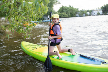 A 10-year-old boy in a life jacket rides a SUP board on the river alone