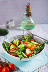 Fresh salad of cucumbers, cherry tomatoes and mint leaves in a bowl on the table vertical view