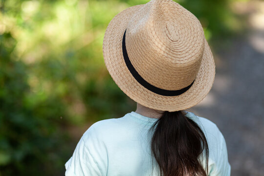 Back view of a girl wearing a straw hat standing in the park